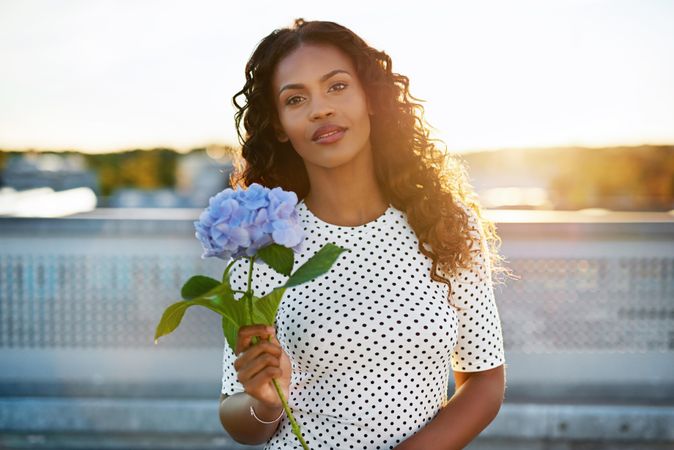 Beautiful Black woman holding out a blue flower on the roof