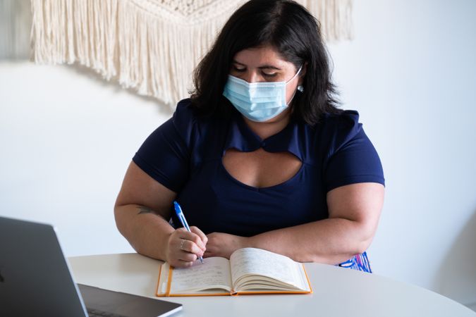 Woman in medical face mask writing notes in a bright modern office