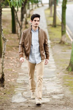 Man in khakis and button up shirt walking on tree lined path