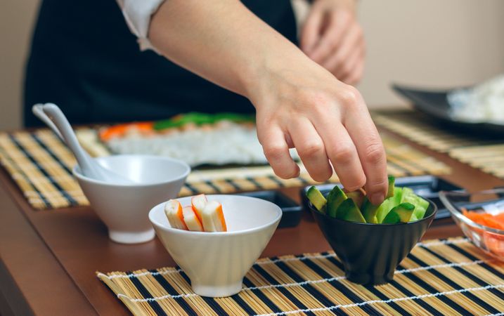 Unrecognizable female chef taking sliced avocado from among the ingredients prepared to make sushi