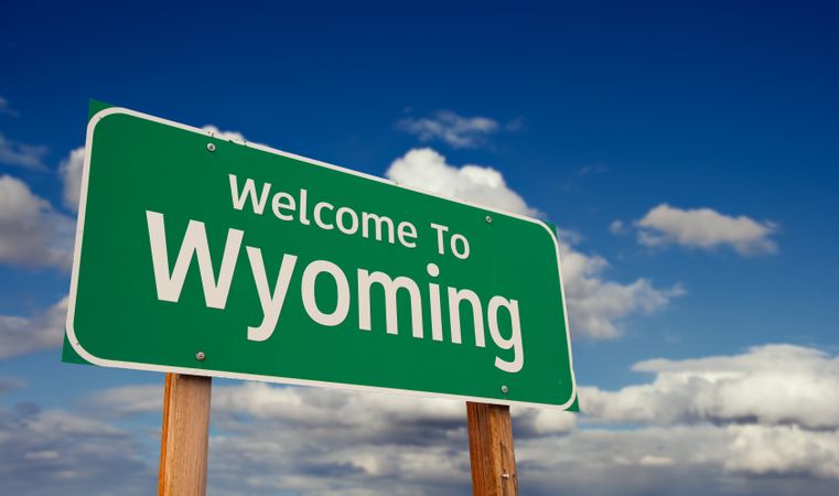 Welcome To Wyoming Green Road Sign Over Blue Sky with Some Clouds.