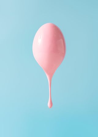 Egg dripping with pastel pink pain on blue background