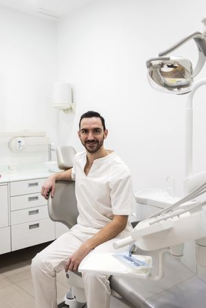 Portrait of a bearded dentist smiling at camera sitting in clinic chair, vertical