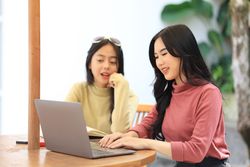 Happy Asian Women Sitting at Outdoor Coffee Shop Looking at Laptop Computer