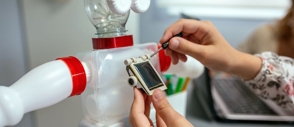 Female student screwing solar panel on recycled toy robot in a robotics class