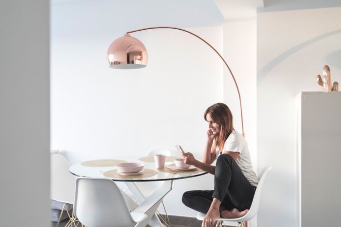 Woman sitting at sunny breakfast table texting on phone in front of cereal bowl