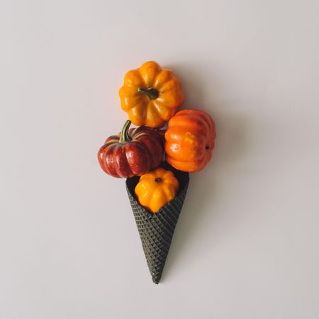 Pumpkins in ice cream cone on light background