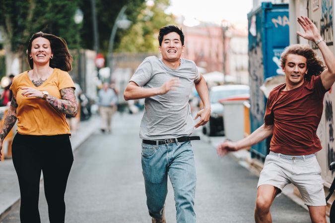 Funny multiracial friends having fun and running along city street