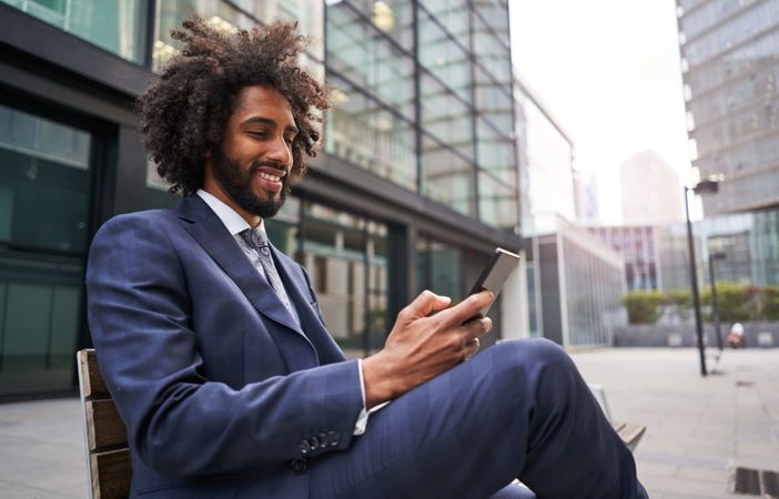 Joyful man in suit sitting outside and messaging