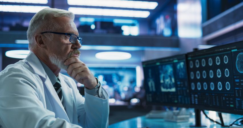 Cancer Research Center Medical Laboratory: Male Neuroscientist Using Desktop Computer To Analyze CT Scans Of Human Brain.
