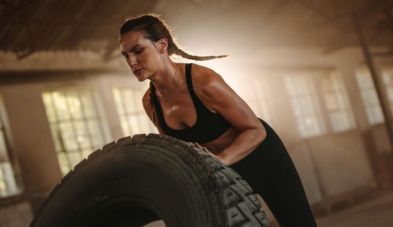 Strong woman working out with a huge tire in cross workout space