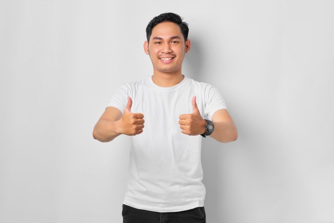 Asian male in grey studio making thumbs up with both hands
