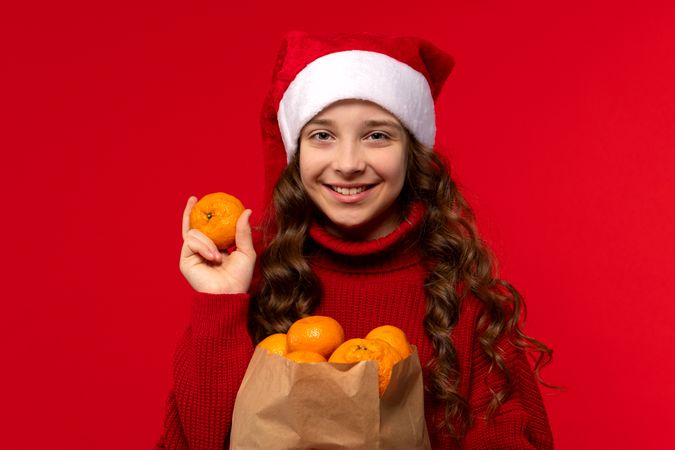 Cheerful girl in Santa hat holds an orange