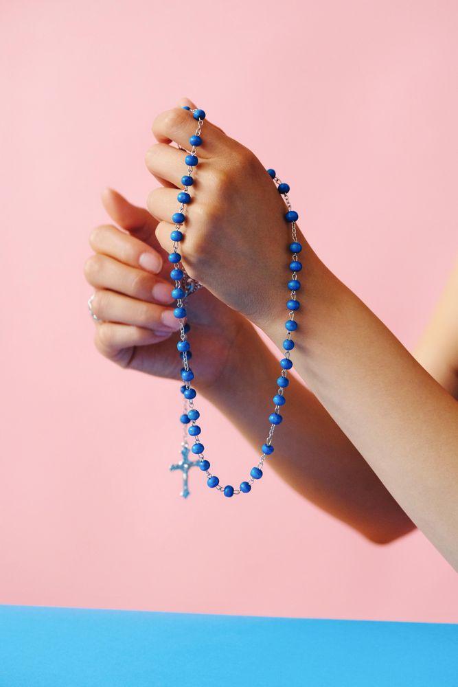 Hands holding rosary beads in pink room with blue table