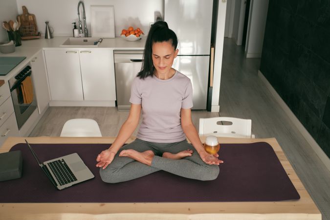 Woman meditating with beer near laptop