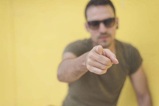 Male pointing at camera in front of yellow wall outside