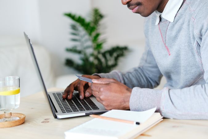 Crop Black buyer with debit card shopping online on laptop