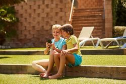 Cheerful boys browsing smartphone sitting on garden