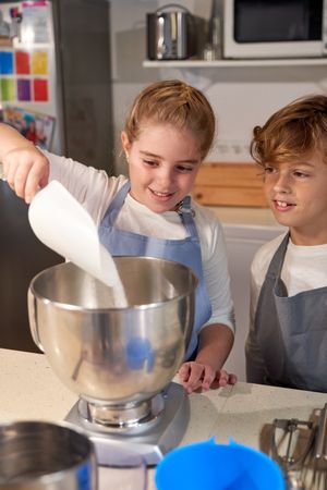 Adorable kids pouring sugar into mixer bowl during dessert prepa