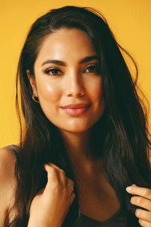 Hispanic woman looking at camera in yellow room with her hands up to her hair