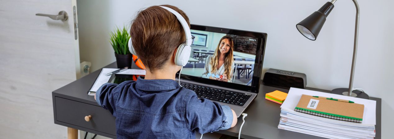 Unrecognizable boy with headphones receiving class at home with