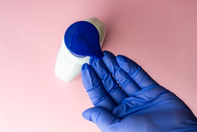 Looking down at pink table with hands in blue latex gloves pumping soap