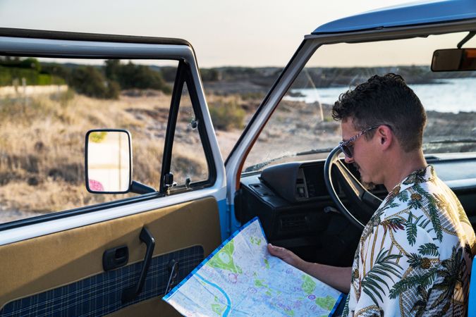 Adult man planing route for road trip while sitting in car on shore