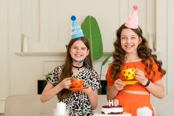 Two girls in birthday hats holding colorful cups