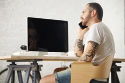 Tattooed man in blank t-shirt speaking on mobile phone