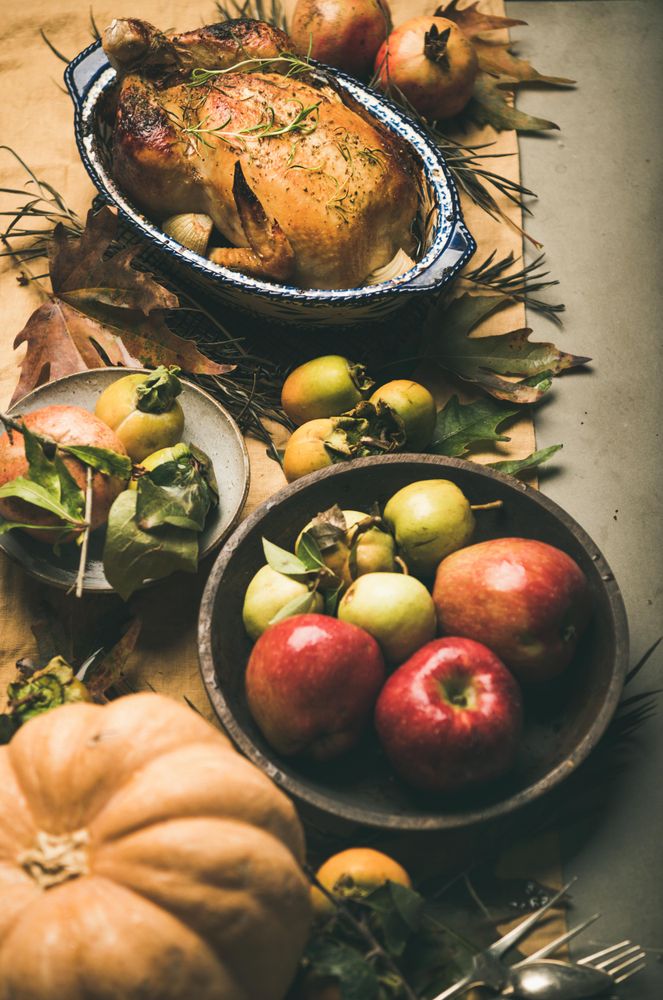 Roast turkey in decorative roasting pan, on table with fall leaves and fruit, vertical composition