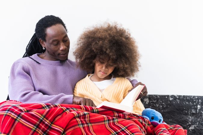 Black father reading book with daughter under plaid