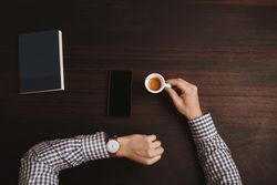 Top view of man checking watch with espresso shot, cell phone and notebook