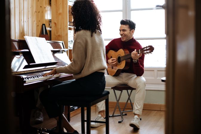 Woman playing piano near man playing guitar in studio
