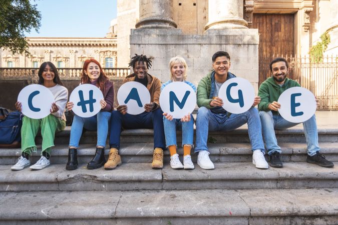 Group of diverse students holding letters spelling 'CHANGE', advocating for social causes on campus steps