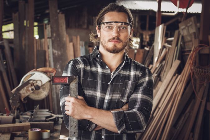 Portrait of male woodworker wearing protective glasses and holding tool in his workshop