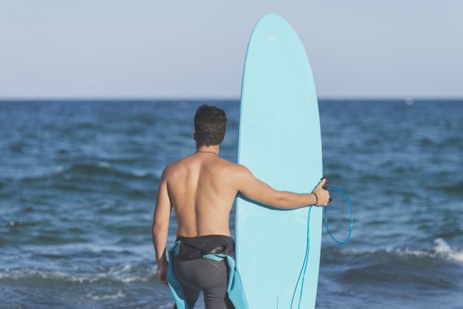 Male surfer with blue board standing in front of the water