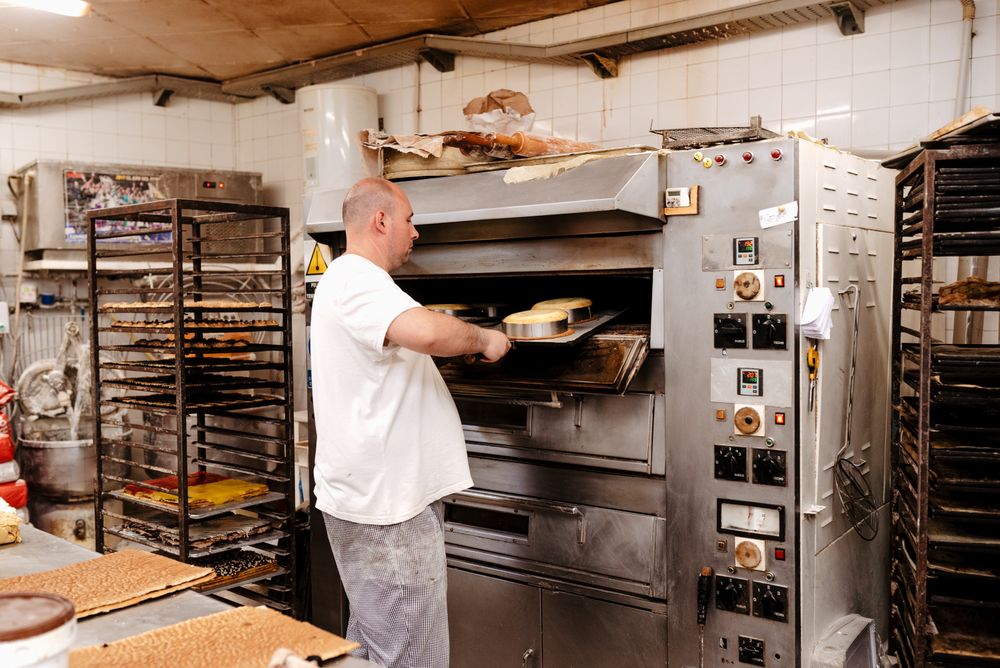 Male baker putting cakes into oven