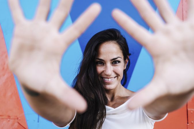 Smiling woman leaning against a wall while framing the face with hands