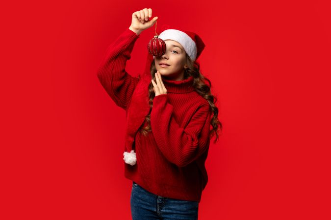 Teen girl in Santa hat posing with red Christmas ornament.