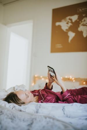 Woman lying down on bed with smartphone