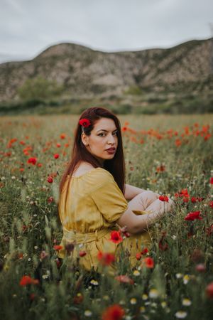 Woman sitting in field with poppies and daisies