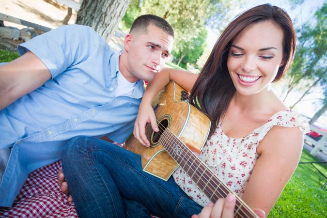 Woman Playing Guitar with Boyfriend In The Park.