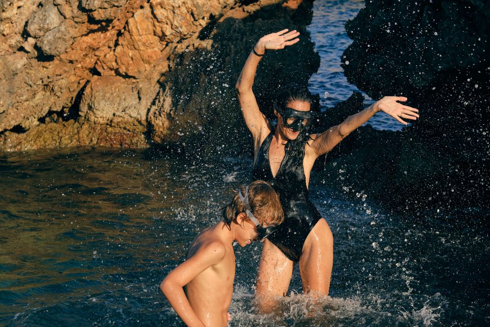 Cheerful mom with son having fun with splattering sea water
