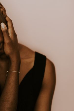 Woman wearing a dark tank top with gold bracelet holding her face