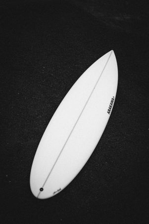Surfboard lying on dark sand, vertical