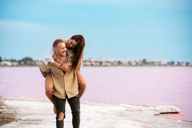 adorable couple giving a piggyback ride on an amazing beach of pink water