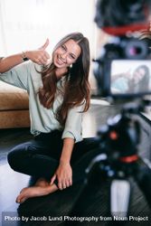 Smiling woman sitting on floor recording content on camera 48jv70