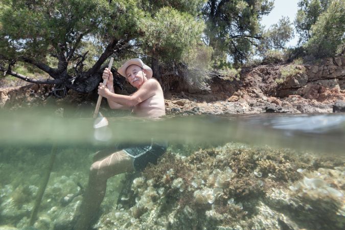 Man sitting on sea hill with stick in hands