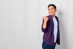 Asian male in grey studio with pointing thumb to the side