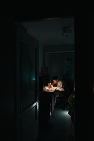 Young man studying with desk lamp in dark room
